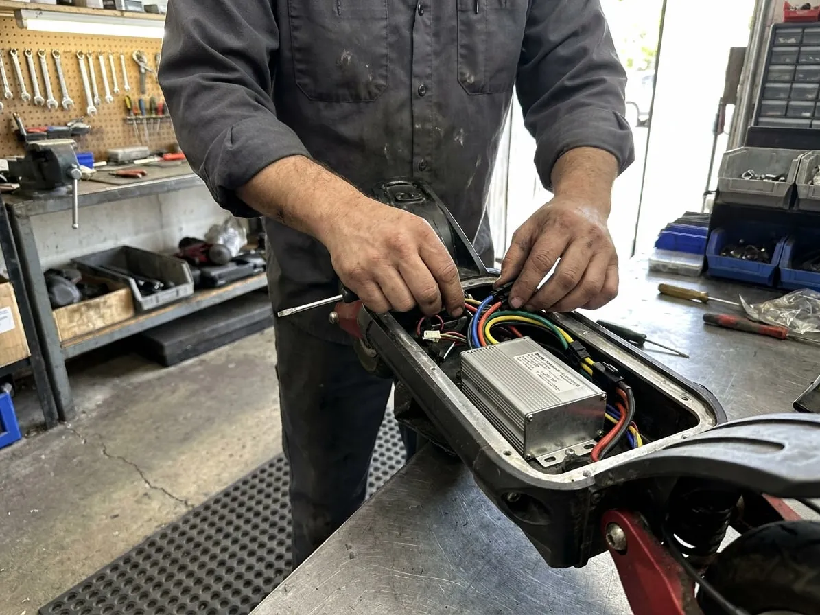 Technician reconnecting the motor controller inside the open deck of an electric scooter