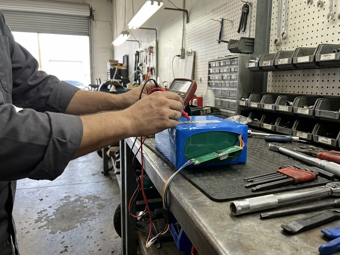 Technician measuring cell groups of a scooter battery pack with multimeter probes, the BMS board visible at the end