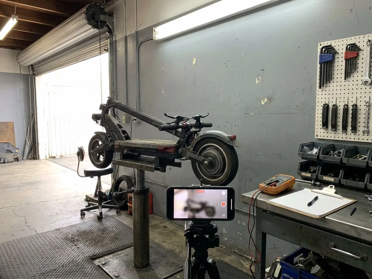 Phone on a tripod recording an electric scooter wheel spinning on a repair stand during its final test