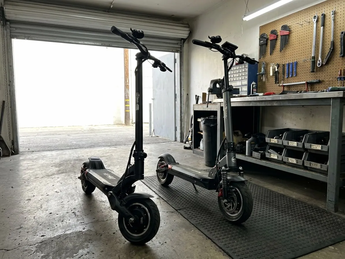 Two premium electric scooters standing side by side in a repair workshop